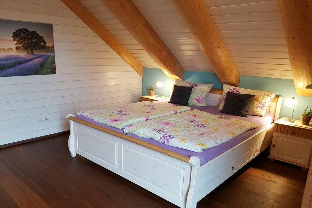 Een slaapkamer met een houten plafond, een bed met bloemenbeddels, nachtkastjes met lampen en een aan de muur hangend schilderij.
