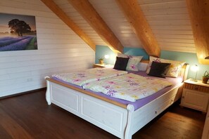 Een slaapkamer met een houten plafond, een bed met bloemenbeddels, nachtkastjes met lampen en een aan de muur hangend schilderij.