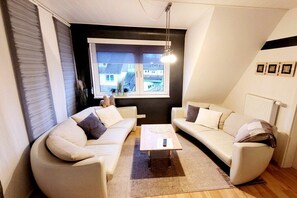 A modern living room with two white sofas, a coffee table, and a large window with a view of buildings. - Holiday apartment with 2 bedrooms (Hessisch Lichtenau)