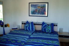 Ein Schlafzimmer mit einem Bett, einem Nachttisch, einer Vase mit Blumen und einem gerahmten Gemälde an der Wand.
