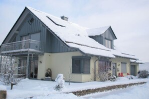 Une maison à deux étages avec un balcon, un toit enneigé et un mur de pierre à l’avant.