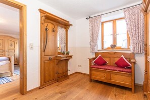 Ein hölzernes Bett mit roten Kissen, ein Holzschrank und ein Fenster mit blumigen Vorhängen.