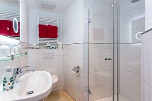 A modern bathroom with a glass shower enclosure, a white sink with a mirror above it, and a red towel hanging on the wall. - Holiday apartment with 1 bedroom (Bad Reichenhall)