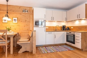 Eine kleine Küche mit weißen Schränken, einer Mikrowelle, einer Kaffeemaschine und einem Holztisch mit Stühlen.