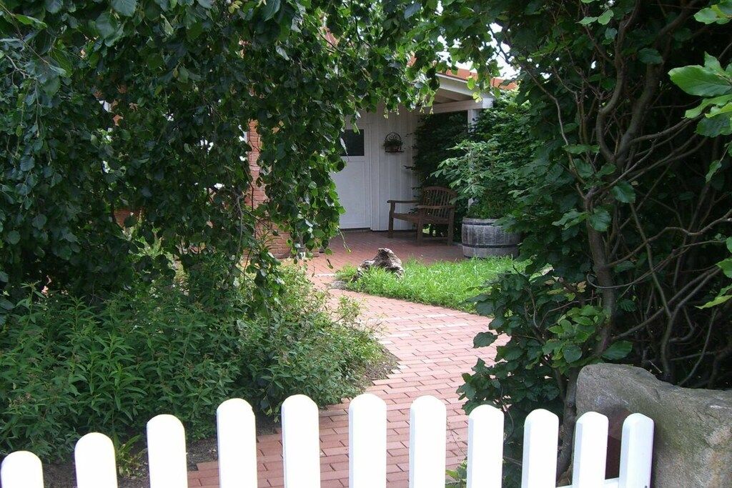 Un sentier de jardin qui mène à un patio couvert, agrémenté d’un banc et d’un jardinière.