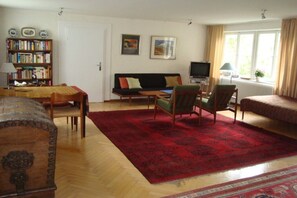 A living room with a sofa, chairs, a coffee table, a bookshelf, a television, and a window with curtains. - Apartment in Lindau with swimming pool (Lindau)
