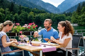 A dining table with a meal, surrounded by chairs, set against a backdrop of a lake and mountains. - Holiday apartment with 1 bedroom (Bayerisch Gmain)