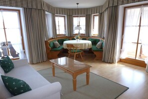 A room with a white sofa, a wooden coffee table, a round table with chairs, and a green sofa with cushions. - Holiday apartment with 1 bedroom (Bayerisch Gmain)