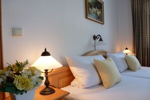 A hotel room with a bed, two bedside lamps, a nightstand with a vase of flowers, and a painting on the wall. - Holiday apartment with 1 bedroom (Bayerisch Gmain)
