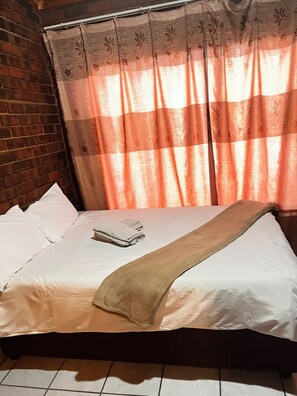 A bed with white linens, a brown throw blanket, and a folded towel.