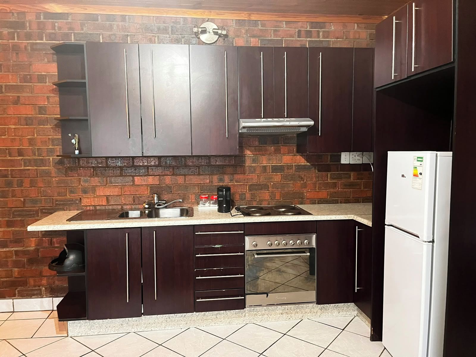 Una cocina con armarios de madera oscura, un lavamanos de acero inoxidable, un horno empotrado y un refrigerador blanco.