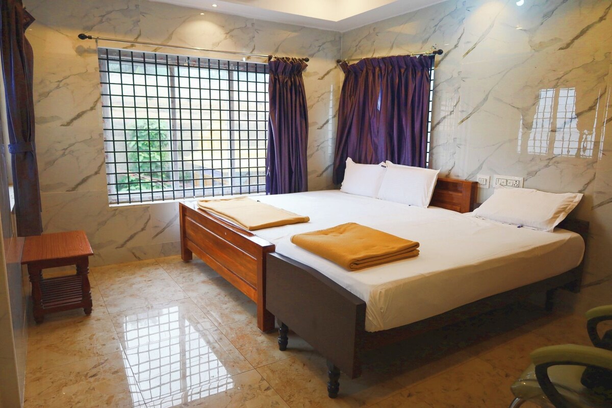 Un dormitorio con una cama, cortinas, un ventanal con celosías y un taburete de madera pequeño.