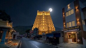 Un templo con una gran luna en el cielo, una calle en primer plano y un edificio con un letrero que dice 'Maruti Residency'.