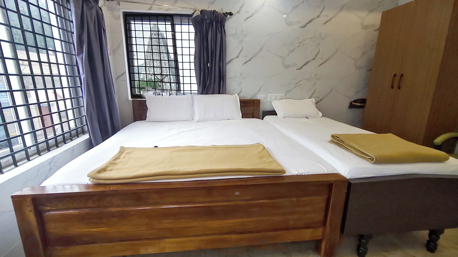 A hotel room with a wooden bed, white bedding, a window with metal bars, and a marble-patterned wall.