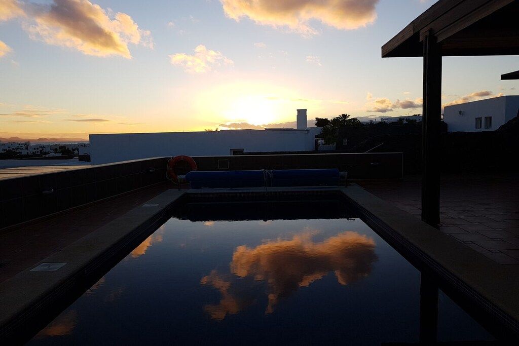 Une piscine sur le toit offrant une vue dégagée sur le coucher de soleil et les nuages se reflétant dans l’eau.