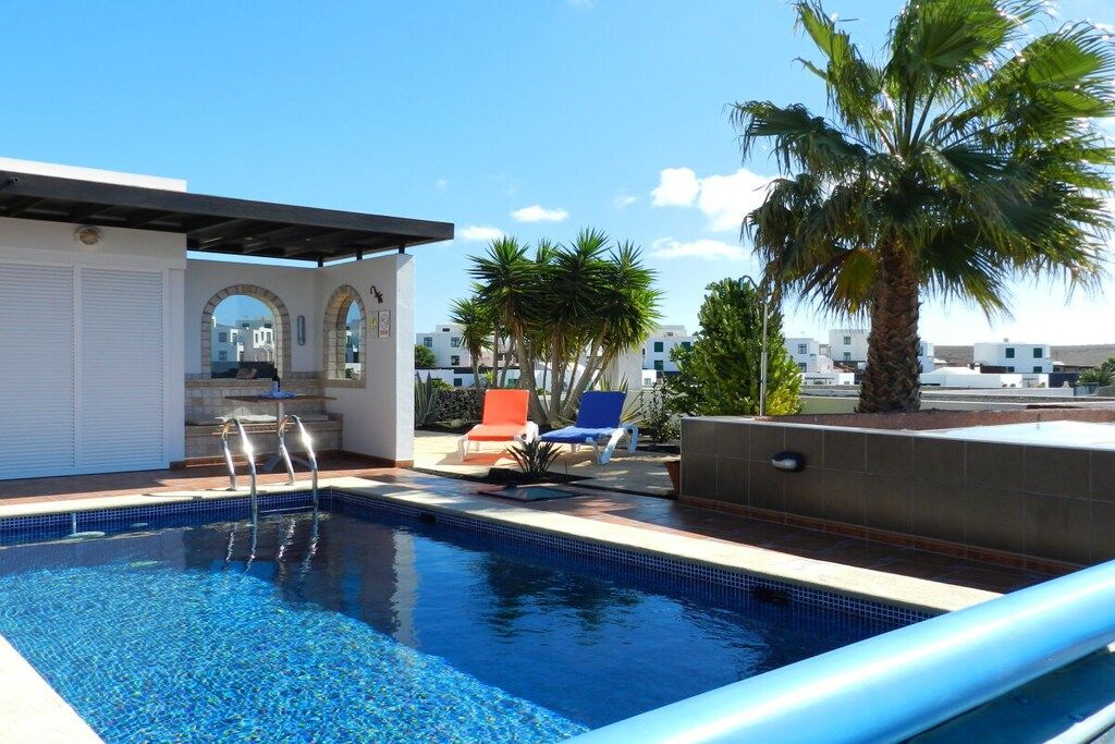 A swimming pool with a clear blue water, surrounded by lounge chairs and palm trees.