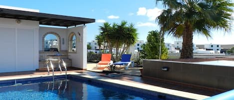 A swimming pool with a clear blue water, surrounded by lounge chairs and palm trees.