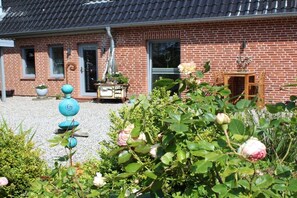 Una casa de ladrillo con techo de tejas, un jardín de rosas y mobiliario de exterior.