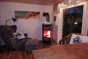 A cozy room with a fireplace, a sofa, a chair, and a large window. - Holiday home with 4 bedrooms (Osterhever)
