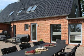 A brick house with a tiled roof, outdoor seating area, and a table with chairs. - Holiday home with 4 bedrooms (Osterhever)