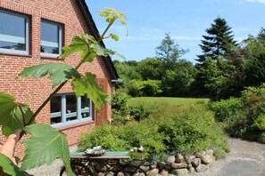 A brick house with a garden, a stone wall, and a wheelbarrow. - Holiday home with 4 bedrooms (Osterhever)