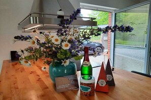 Una mesa con un jarrón de flores, una botella de vino, un tarro de frutos secos y un juego de té.