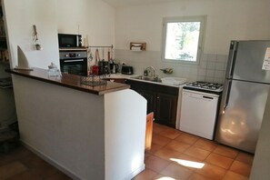 A compact kitchen with a central island, a gas stove, a built-in oven, a microwave, and a refrigerator. - Holiday home in Provence (Merindol)