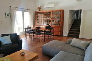 A living room with a sofa, a coffee table, and a dining area with chairs and a cabinet. - Holiday home in Provence (Merindol)