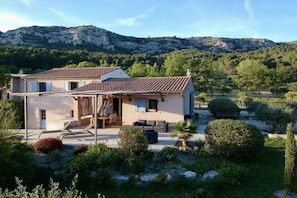 A two-story house with a tiled roof, a patio with outdoor furniture, and a garden with various plants and a small tree. - Holiday home in Provence (Merindol)