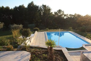 A rectangular swimming pool with a tiled deck, surrounded by a grassy area and trees. - Holiday home in Provence (Merindol)
