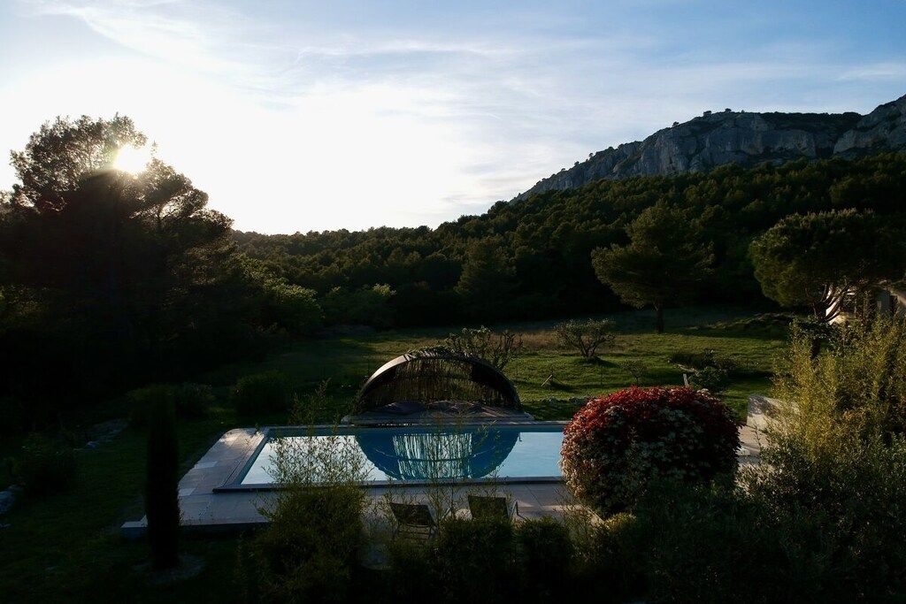 A swimming pool with a glass bottom, surrounded by greenery and a mountain in the background.