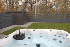 A hot tub with a built-in table and seating area, surrounded by a brick wall and a grassy lawn. - House Comfort by the lake (Göhren-Lebbin)