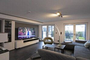 A modern living room with a flat-screen TV, a sofa, a coffee table, and a glass cabinet. - House Comfort by the lake (Göhren-Lebbin)