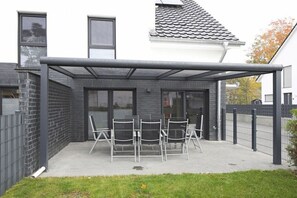 Een overdekt terras met een tafel, stoelen, een glazen deur en een bakstenen muur.