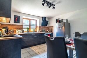 A modern kitchen with dark cabinetry, a built-in oven, and a dining area with a table set for two. - Holiday apartment with 2 bedrooms (Gaißach)