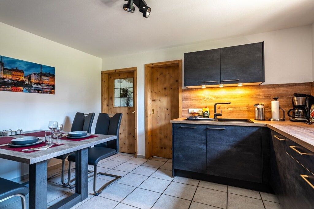 Une cuisine moderne avec des meubles de couleur sombre, un plan de travail en bois et un coin repas avec une table dressée pour deux personnes.