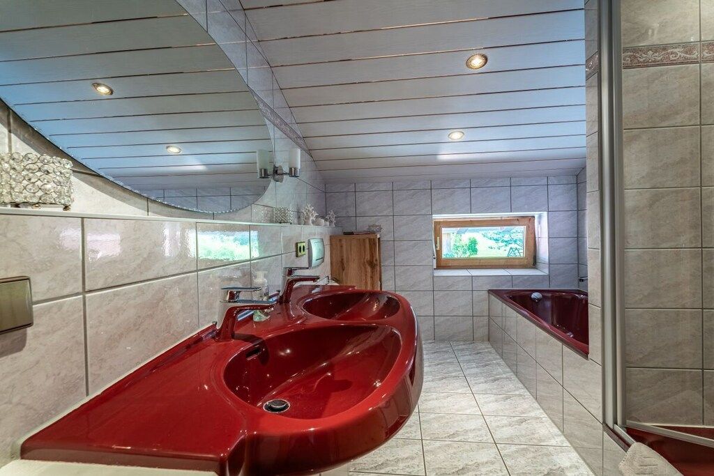A modern bathroom with a large red bathtub, a separate shower area, and a window providing natural light.