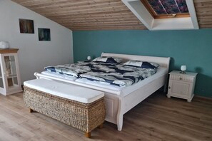 Ein Schlafzimmer mit einem Bett, einem Nachttisch, einer Korbsitzbank und einem Oberlicht.