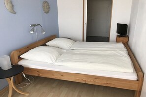 A single bed with a wooden frame, white bedding, a bedside table with a lamp, and a television on a wooden stand. - Holiday apartment with 1 bedroom (Norderney)