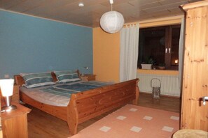 A bedroom with a wooden bed, a nightstand, a lamp, a window with curtains, and a view of the outside. - Holiday apartment with 3 bedrooms (Hallgarten)