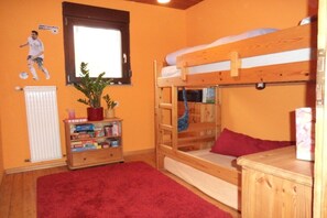 Una habitación con literas, un radiador, una estantería y una ventana.