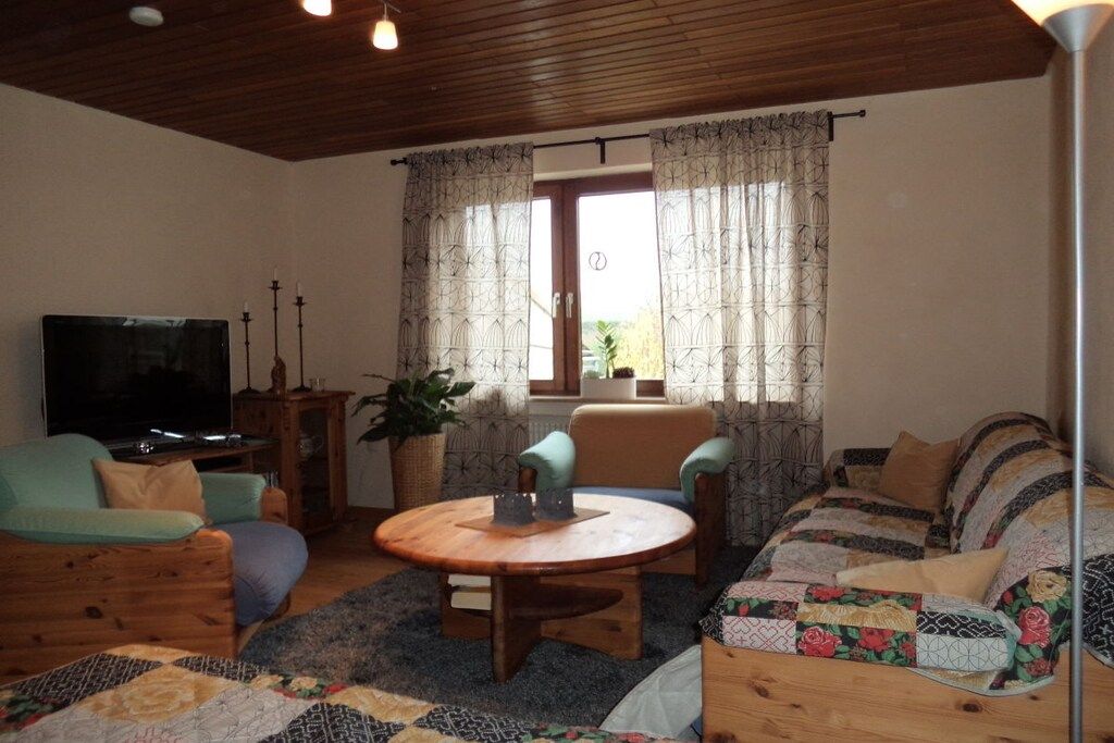 Una sala acogedora con televisión, una mesa redonda de madera y un sofá con cubierta acolchada.