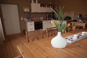 A wooden dining table with a white vase and flowers, a kitchen in the background, and a tray with candles. - Holiday apartment with 3 bedrooms (Hallgarten)