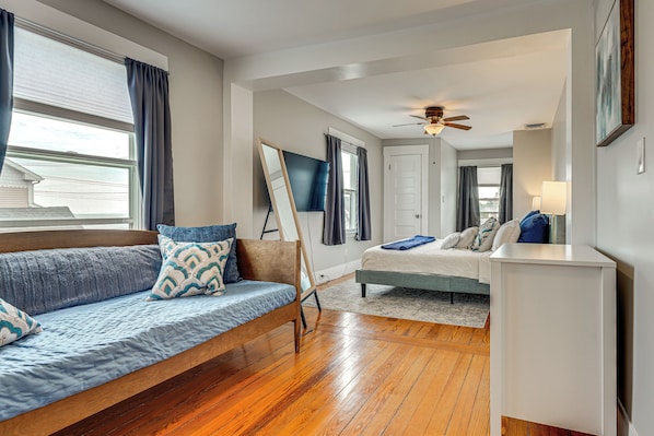 Un dormitorio moderno con piso de madera, cama con colcha de diseño azul y blanco, sofá azul con cojines a juego y un ventilador de techo.