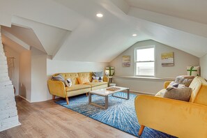 Un loft espaiós amb un sostre alt, un sofà groc, una taula de café i una finestra gran que deixa entrar llum natural.