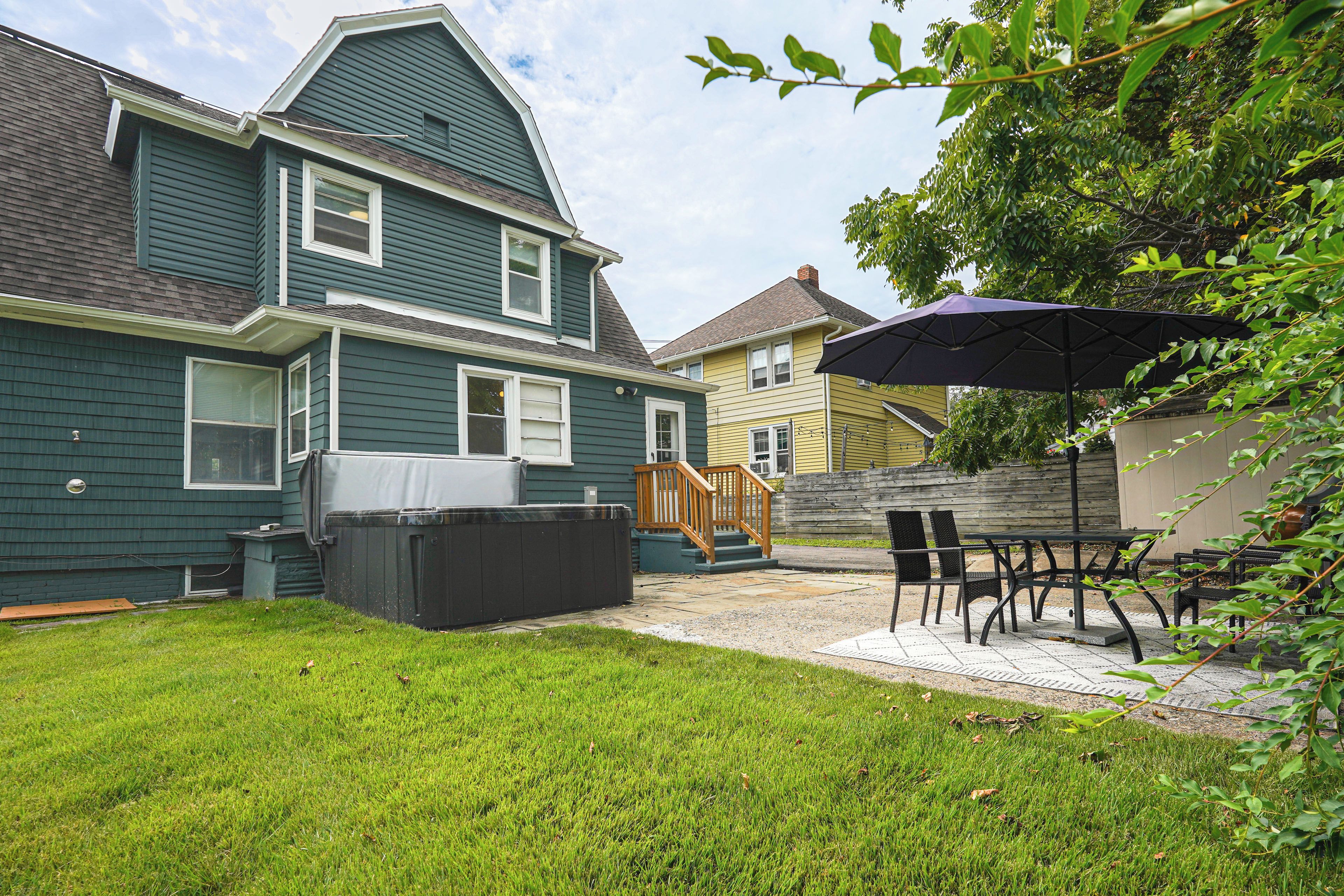 A residential backyard with a covered hot tub, a wooden deck, and outdoor furniture.