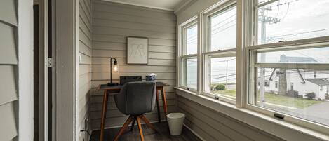A corner room with a desk, chair, and a window overlooking a residential area.