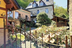 Une cour avec un bâtiment en pierre, une pergola en bois et une rambarde en métal.