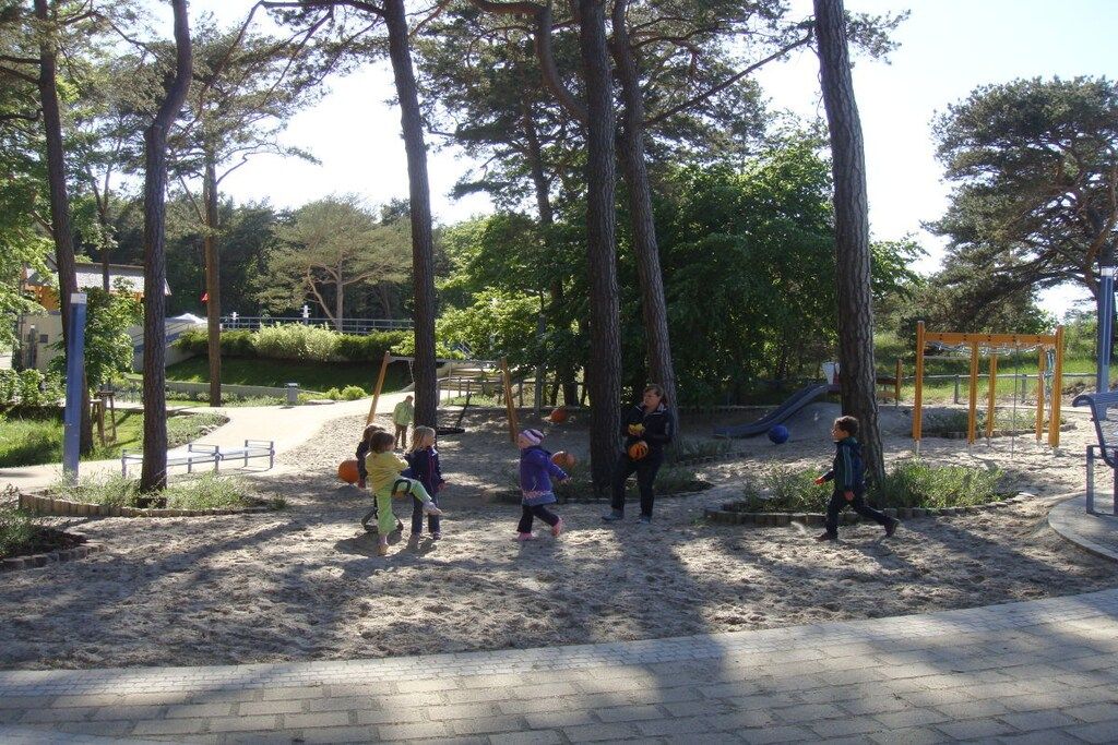 Ein Spielplatz mit Sand, Bäumen und einer Rutsche.