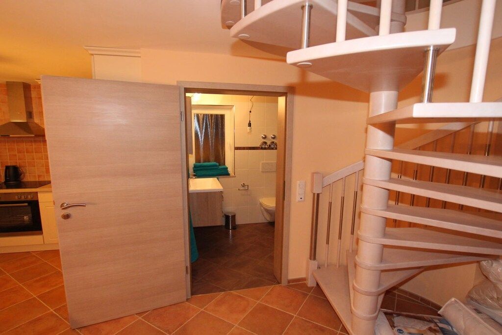 A kitchen with a stove, a sink, and a door leading to a bathroom with a toilet and a shower.